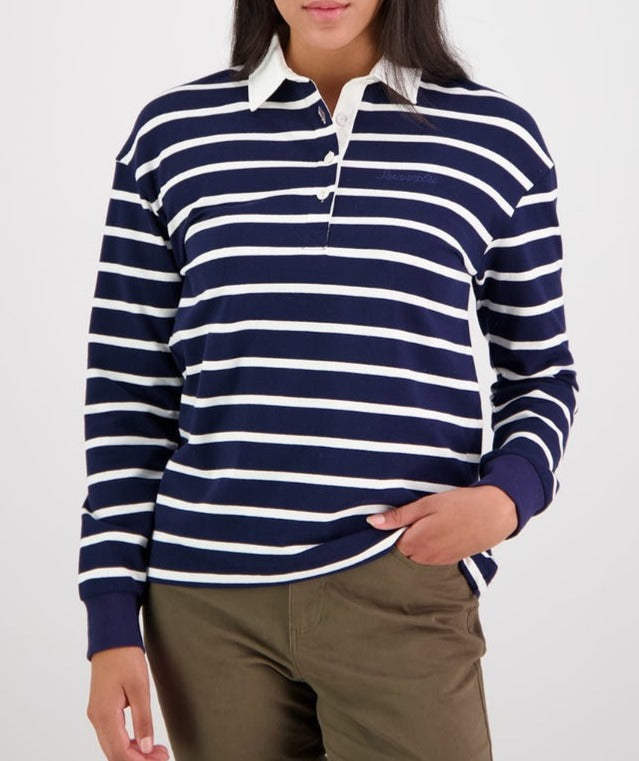 A person wearing the Swanndri Carlaw Rugby, a navy blue and white striped long-sleeve rugby shirt featuring a crisp white collar and three buttons at the neckline. They are also wearing khaki pants with one hand casually tucked into a pocket, embodying the essence of comfortable rugby style.