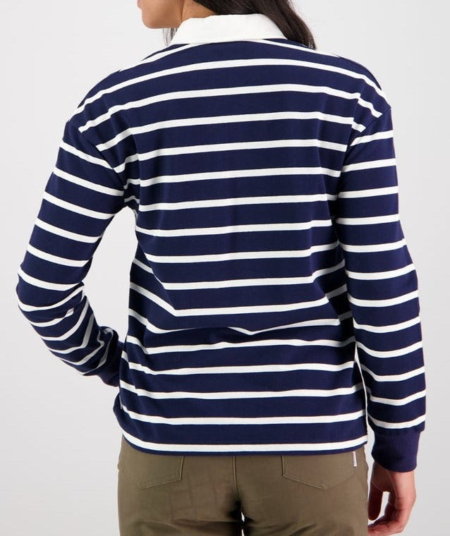 A person wearing the Swanndri Carlaw Rugby—a long-sleeved navy and white striped casual shirt featuring the embroidered Swanndri logo—is shown from the back. They have long dark hair and are paired with olive green pants against a plain white background.