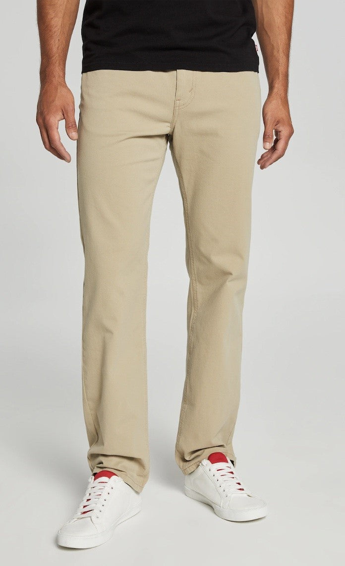 An individual is showcasing the Levis 516 Straight Jean in light khaki and white sneakers with red accents, emphasizing a comfortable fit. The person is featured from the chest down, standing with hands relaxed at their sides against a clean light grey background.