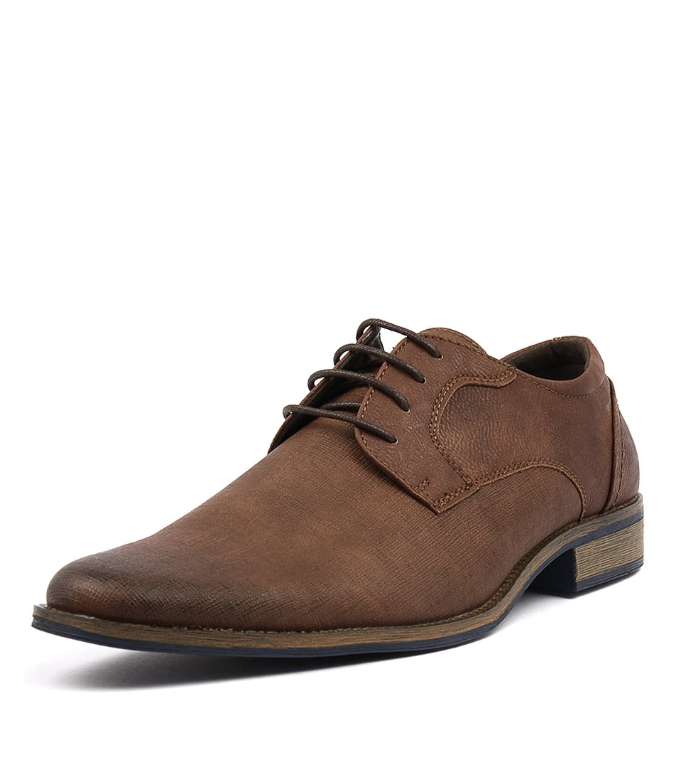 The UNcut Hartley Shoe is a brown leather men's lace-up dress shoe with a closed lacing system, featuring a slightly pointed toe, a low stacked heel, and a textured finish. It has a classic, polished appearance suitable for formal attire and is available in UK sizing.