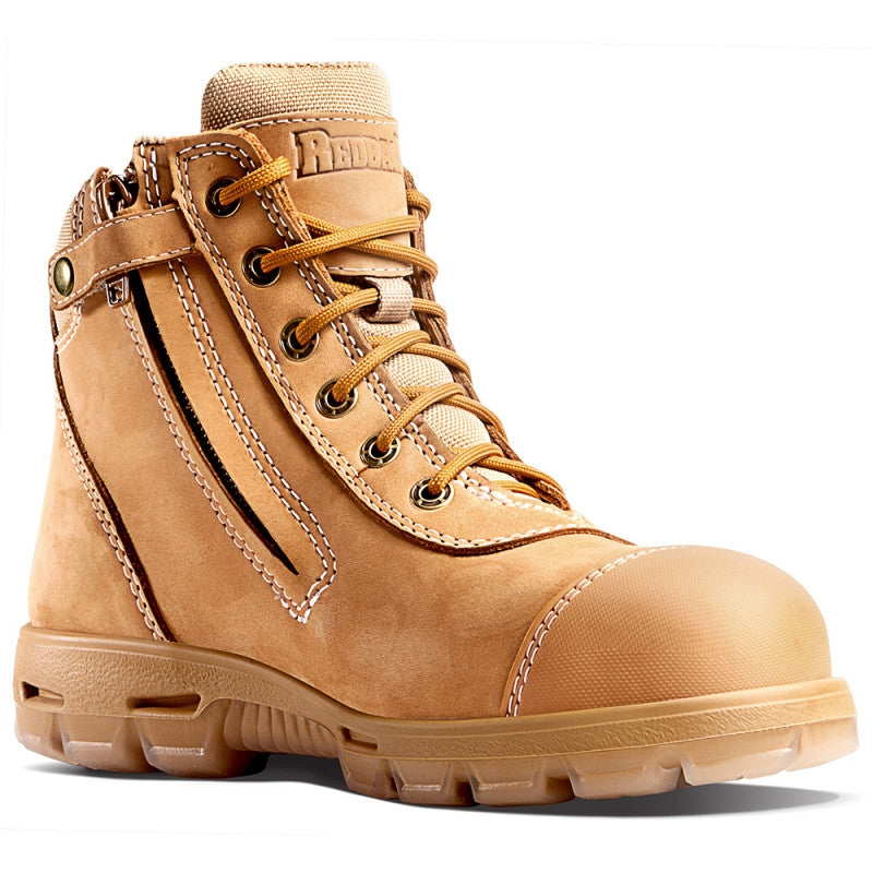 Introducing the Redback Cobar Safety Toe Zip Boot, a tan-colored steel cap work boot with sturdy stitching, reinforced toe, and a convenient side zipper. It boasts metal eyelets for laces, a padded ankle for added comfort, and a rugged TPU outsole designed for durability. An air cushion inner sole provides extra support. The brand name is proudly displayed on the tongue of the boot.