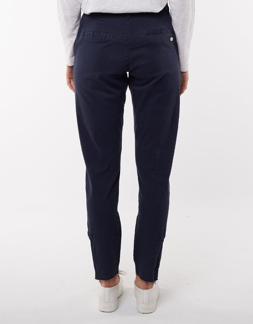 A person wearing dark blue, comfortable Foxwood Liberty Pant and a light-colored long-sleeve top, seen from the back. The pants accentuate a relaxed style. The person is also wearing white sneakers against a plain white background.