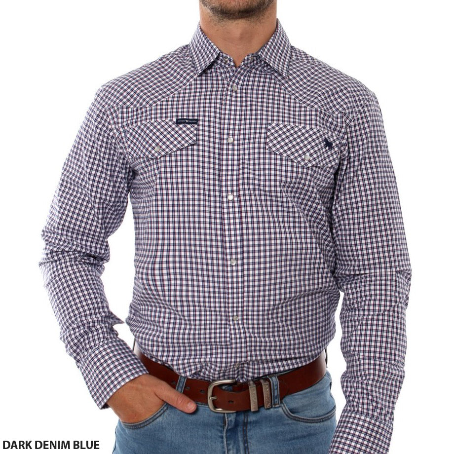 A person wearing a Ringers Western Wyoming Shirt, which is a dark denim blue checkered long-sleeve shirt featuring a collar and two breast pockets. The semi-fitted shirt, made from 100% cotton, is tucked into light blue jeans secured by a brown leather belt. The person's right hand rests in their jeans pocket. "Ringers Western" text is visible at the bottom left of the shirt.